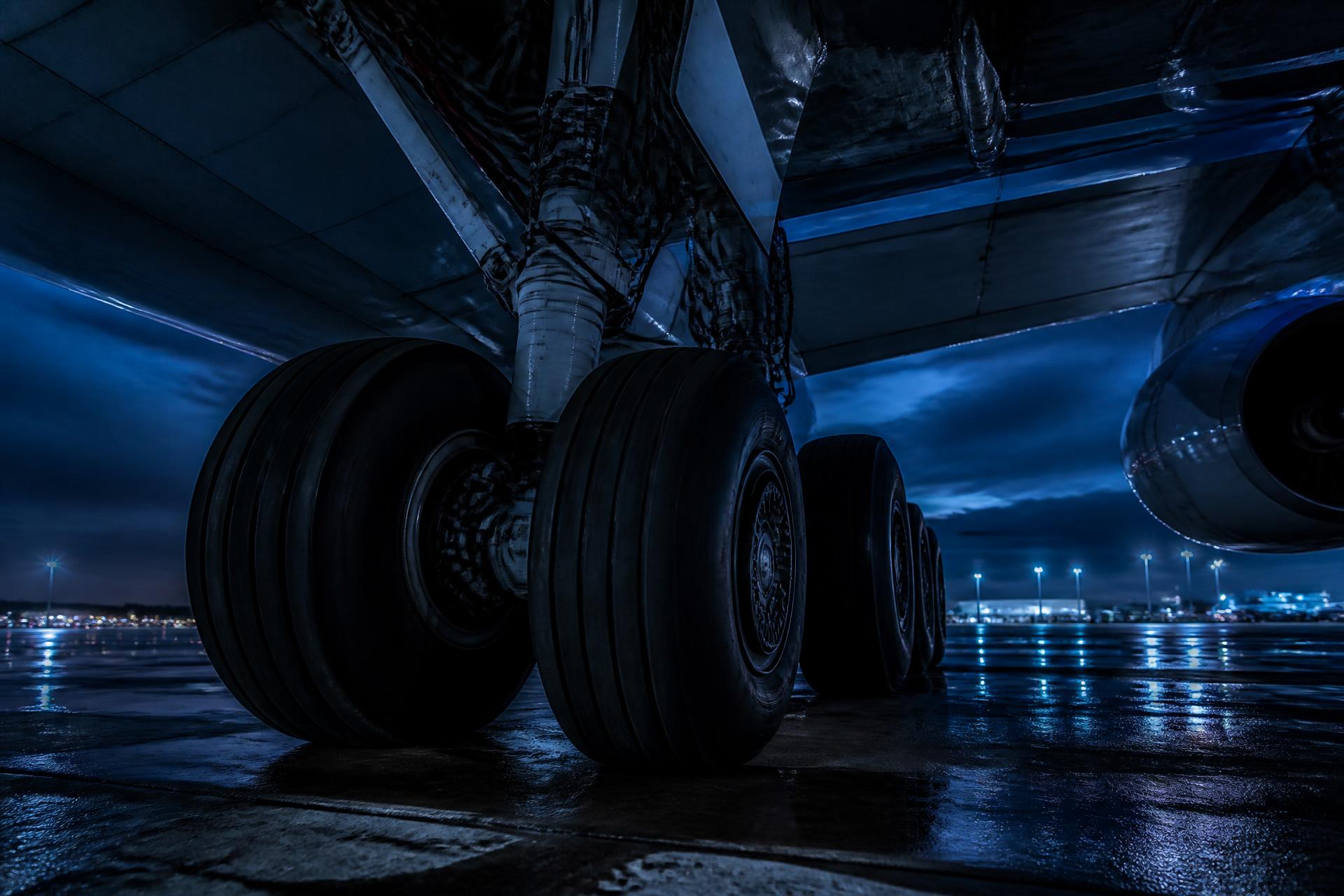 Wide-body aircraft main landing gear and tyres on a wet apron at dusk